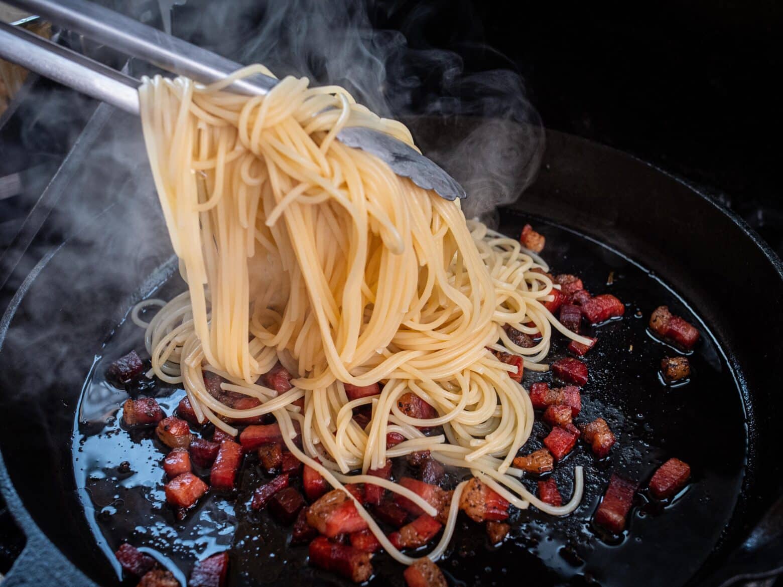 Spaghetti werden zu den Speckwürfeln gegeben