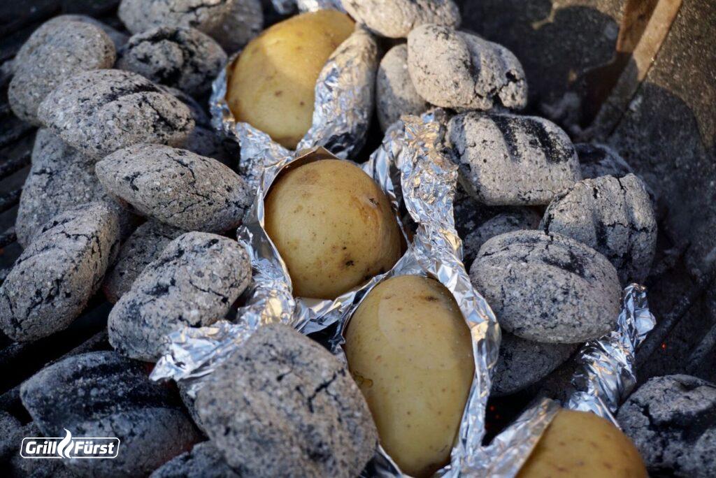 Ofenkartoffeln in Alufolie auf dem Holzkohlegrill in der Glut