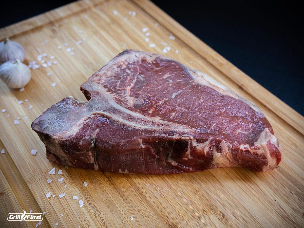 T-Bone Steak roh mit Salzflocken und Knoblauch auf einem Holzbrett zum Grillen