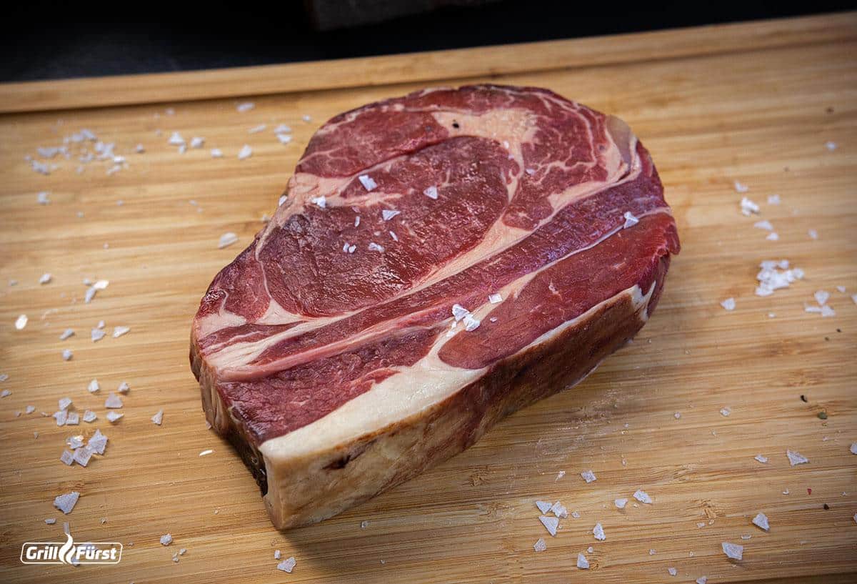 Rib Eye Steak roh mit Salzflocken auf einem Holzbrett