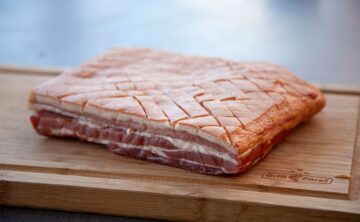 Bauchfleisch vom Schwein mit eingeschnittener Schwarte auf einem Holzbrett