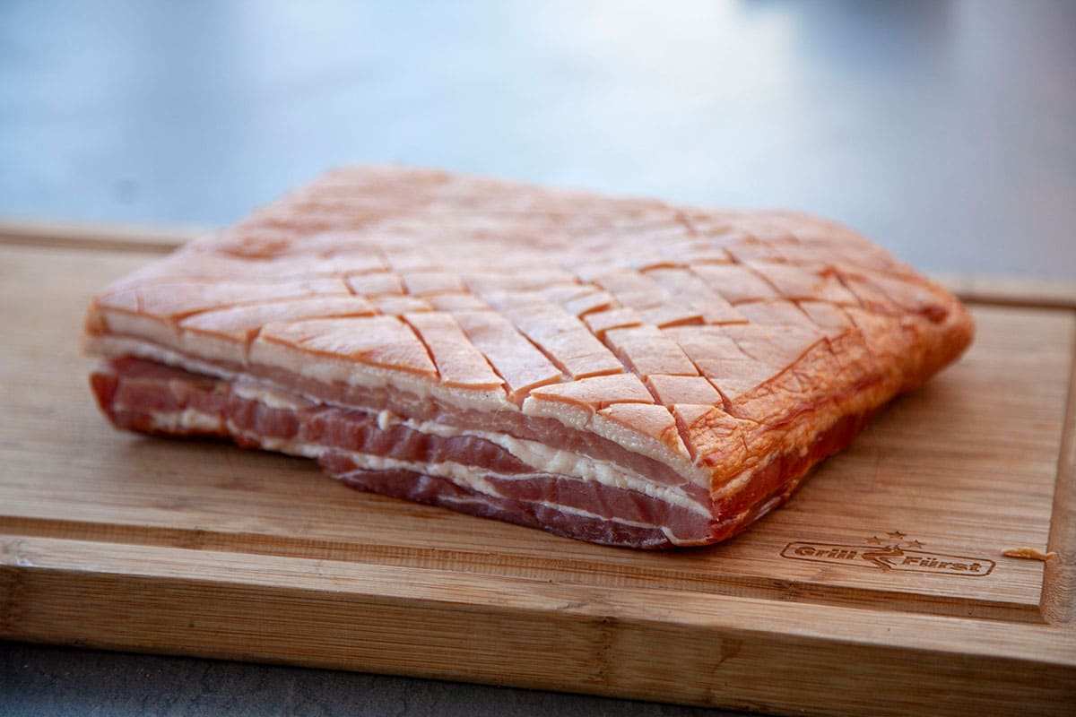 Bauchfleisch vom Schwein mit eingeschnittener Schwarte auf einem Holzbrett