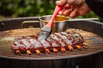 Marinierpinsel mit Silikonborsten zum gleichmäßigen Auftragen von BBQ-Sauce auf saftige Spareribs am Grill Marinierpinsel mit Silikonborsten zum gleichmäßigen Auftragen von BBQ-Sauce auf saftige Spareribs am Grill