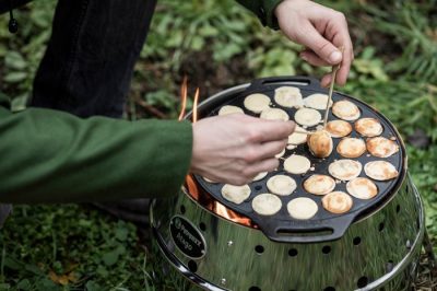Petromax Poffertjespfanne aus Gusseisen auf dem Atago Grill, in der goldbraune Poffertjes mit Holzstäbchen gewendet werden.